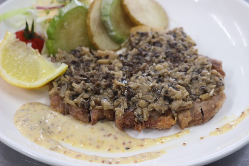 きのこのソースをのせた焼いたお肉に、レモンとサラダを添えた一皿