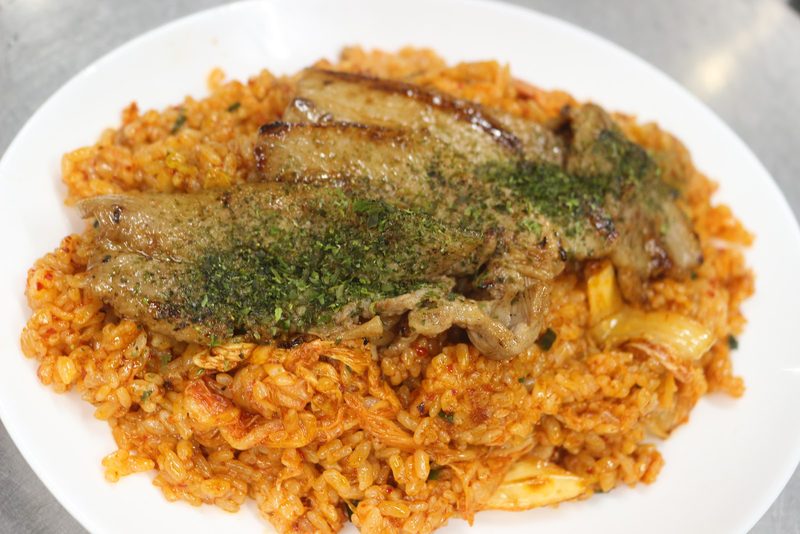 赤く色づいた炒めご飯の上に、青のりをふった焼いた豚肉をのせた一皿