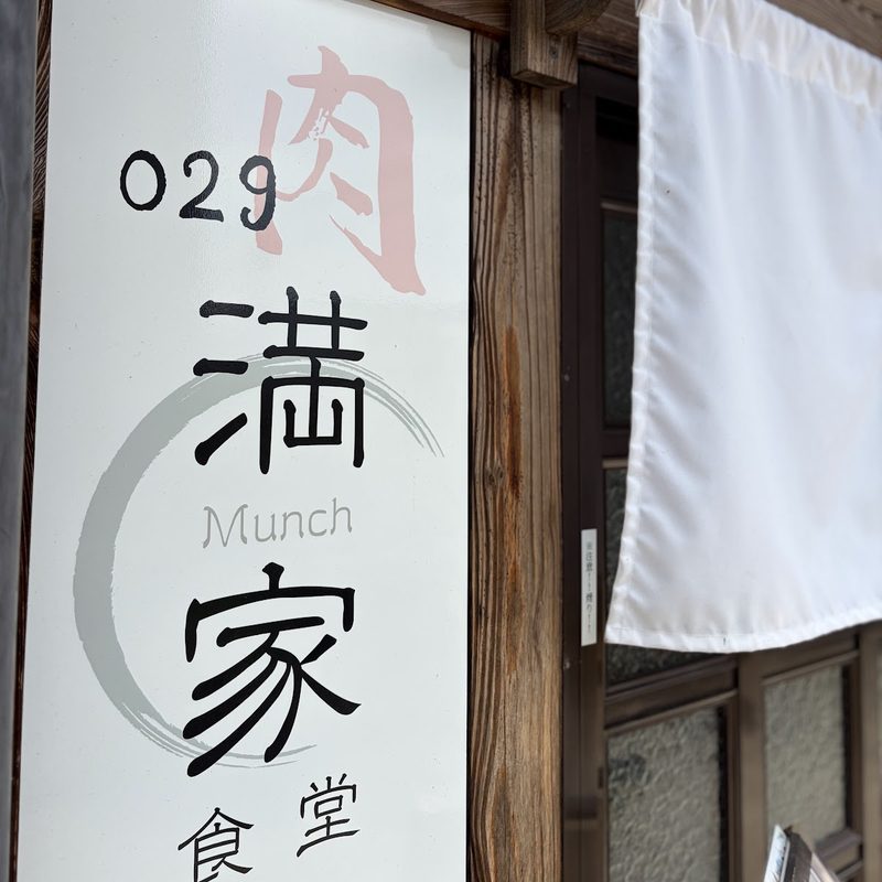 「029 肉 満家 食堂」と書いた縦長の白い看板と、入口の白いのれん