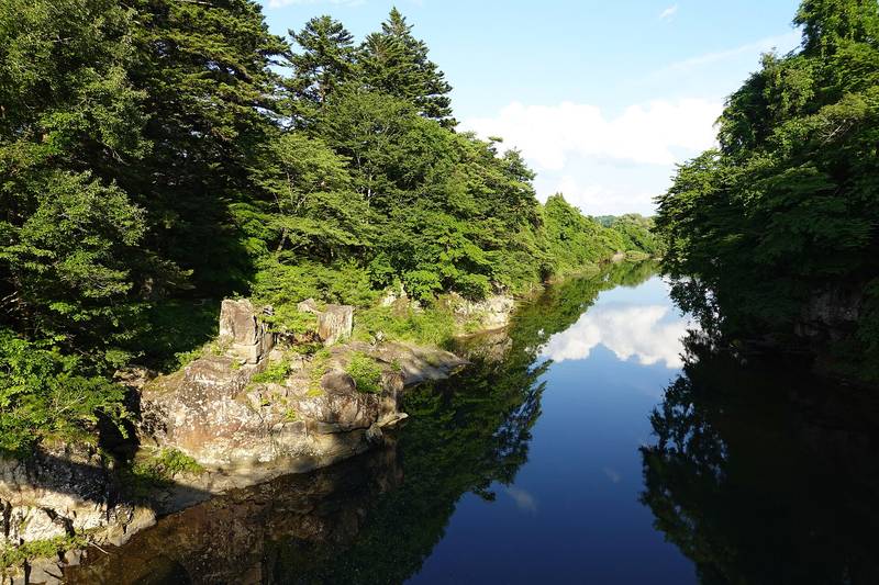 緑の木々に囲まれ、空を映して流れる厳美渓の磐井川